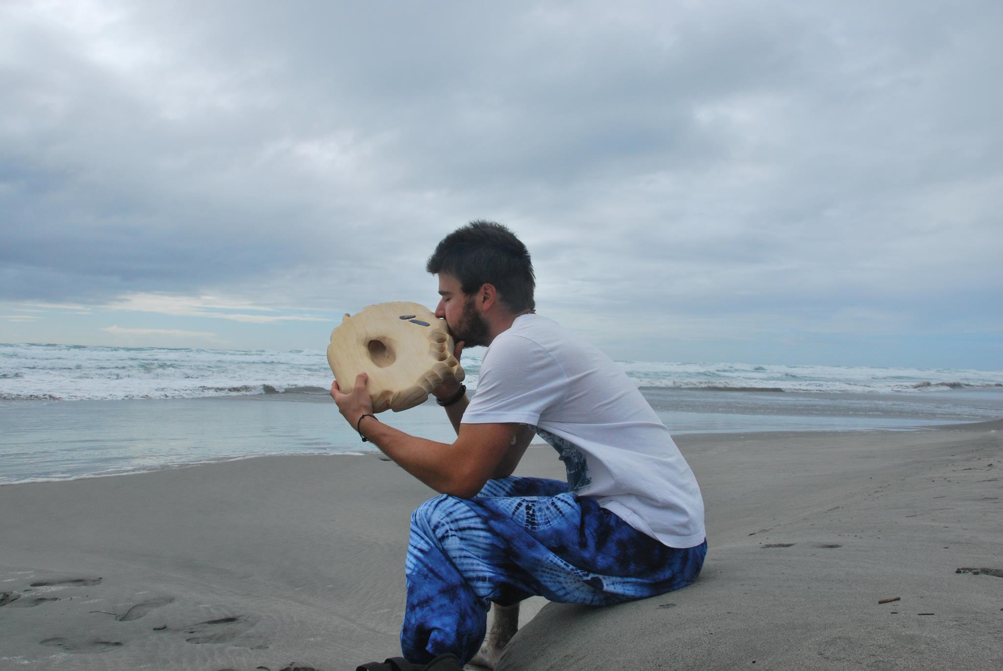 Photo de Julien Doutaz, fabricant des ujazi didgeridoos, sur une plage en Nouvelle Zélande avec un didgeridoo sculpté